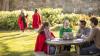 Two groups of students on the grounds of a UK university on a sunny day: in the foreground a group of four students (two females, two males) sitting around a picnic table talking and laughing, in the background two female students in conversation